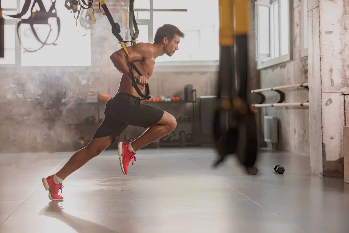 homem treinando com consistência usando trx em uma academia