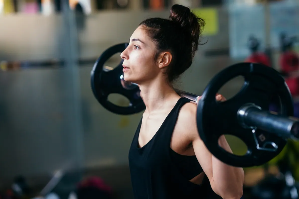 Mulher treinando com barra na academia