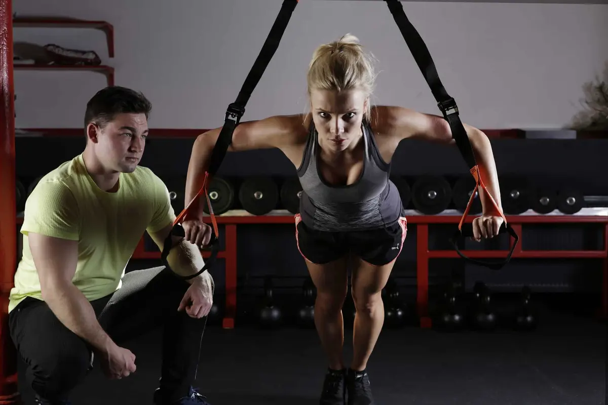 personal trainer acompanhando mulher no TRX