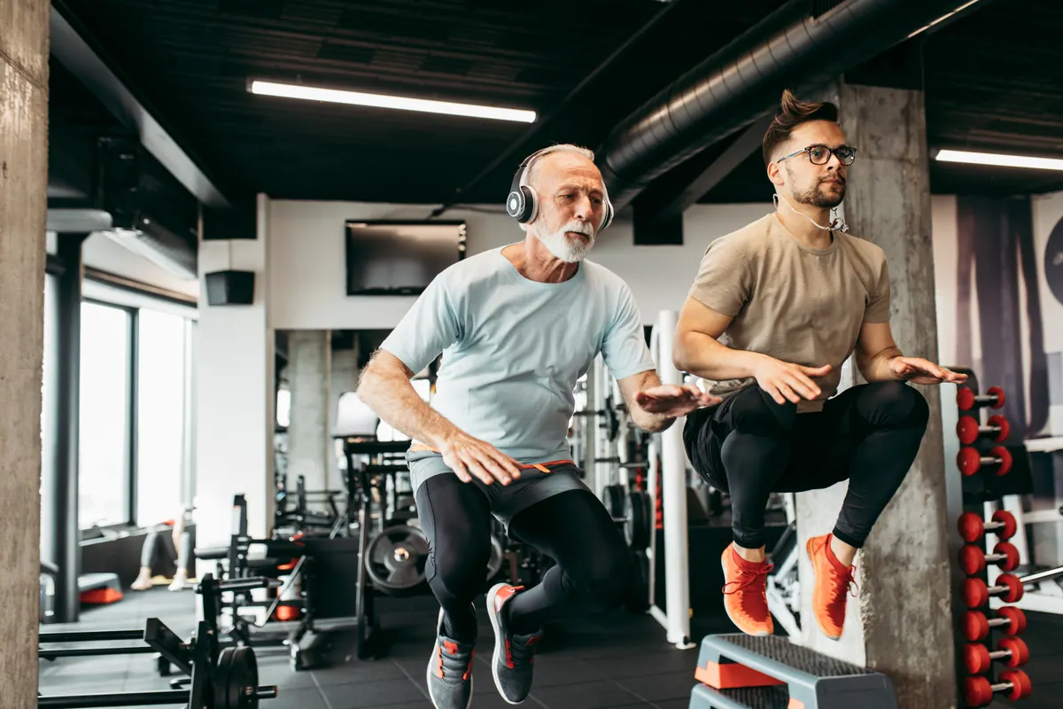 Homem mais velho treinando na academia com o personal trainer