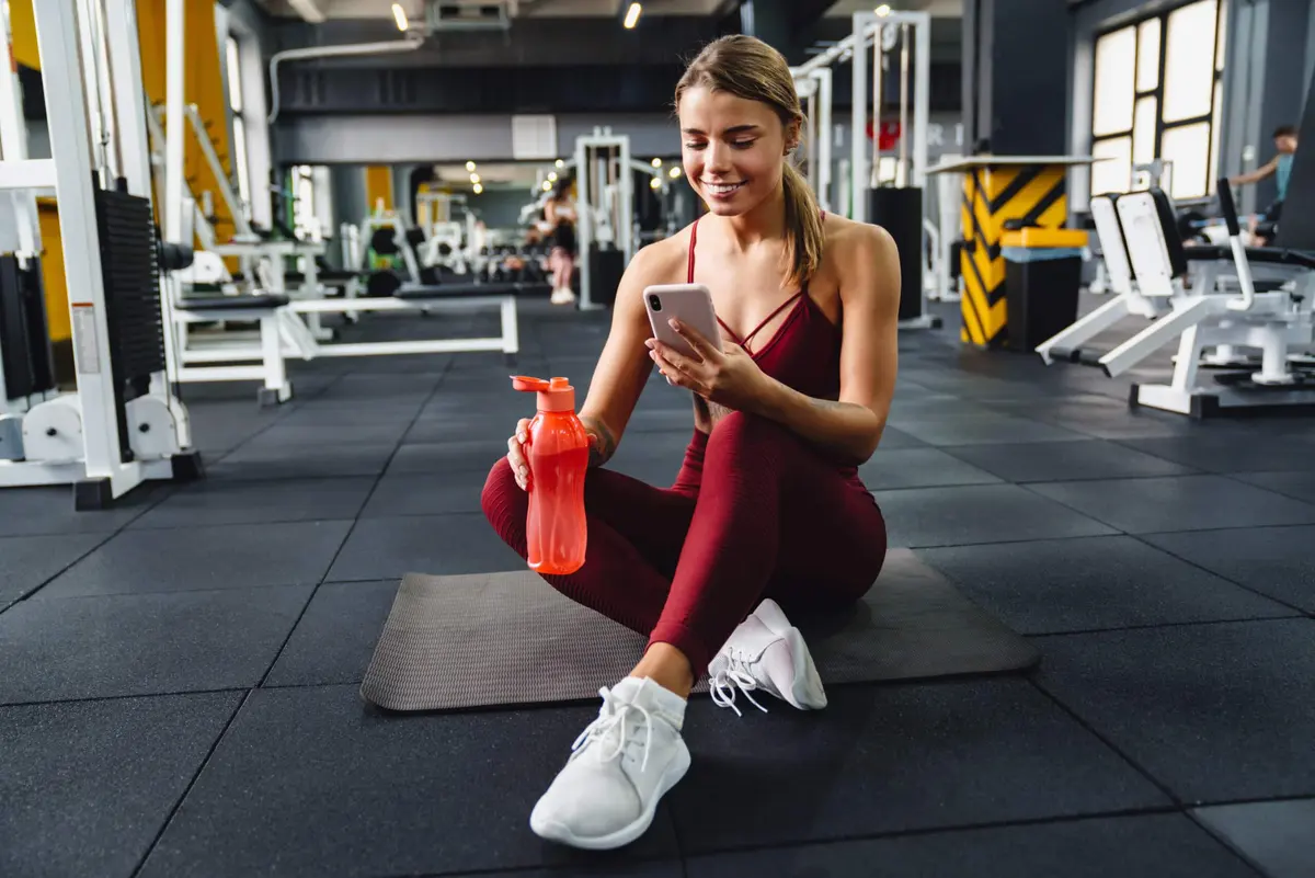 mulher sentada na academia usando o celular