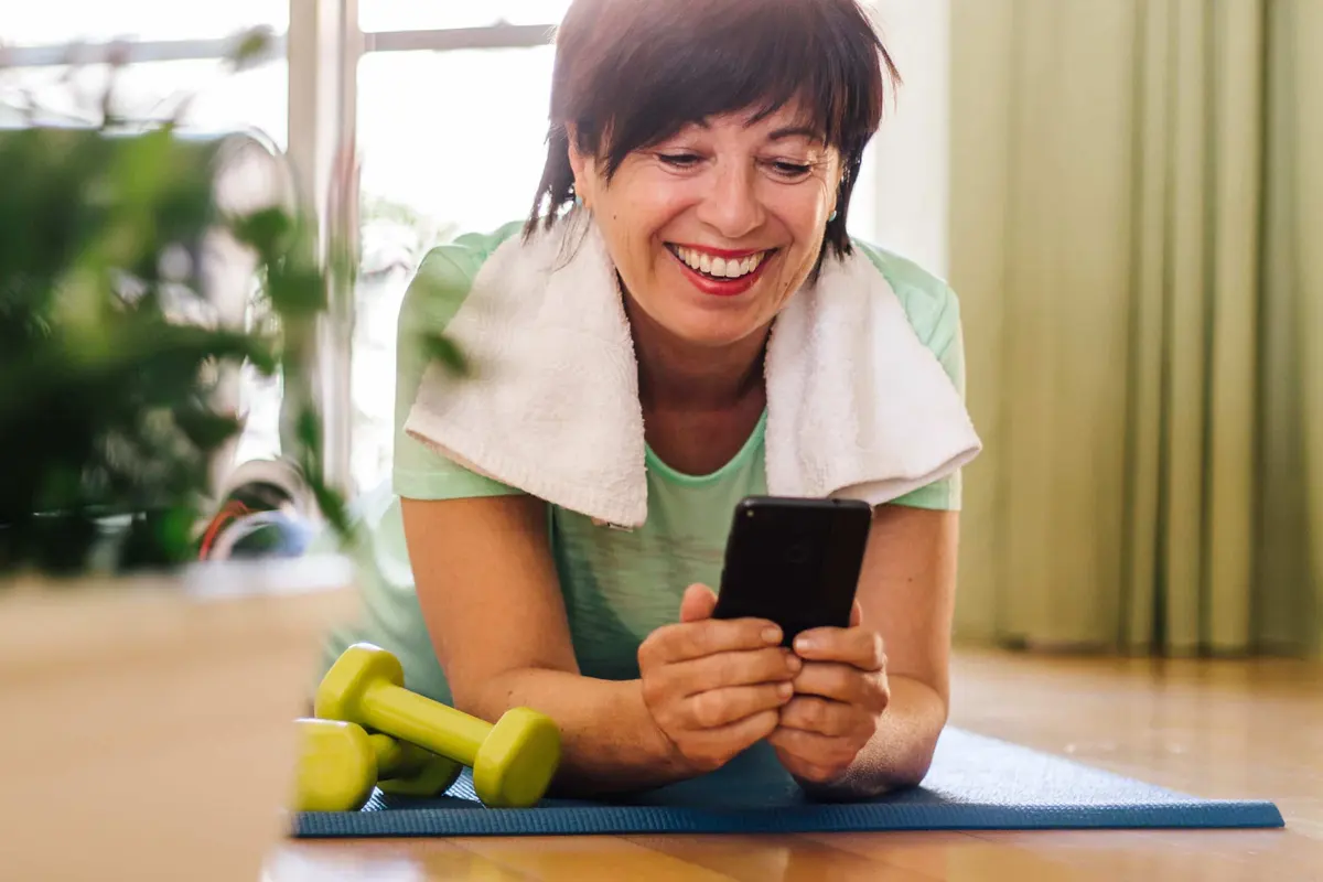 mulher sorrindo com o celular depois do treino em casa