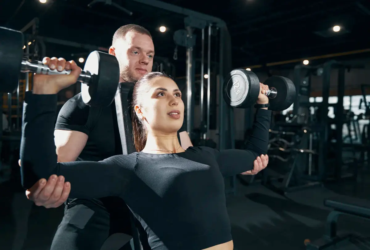 personal trainer corrigindo o desenvolvimento de ombros com halteres
