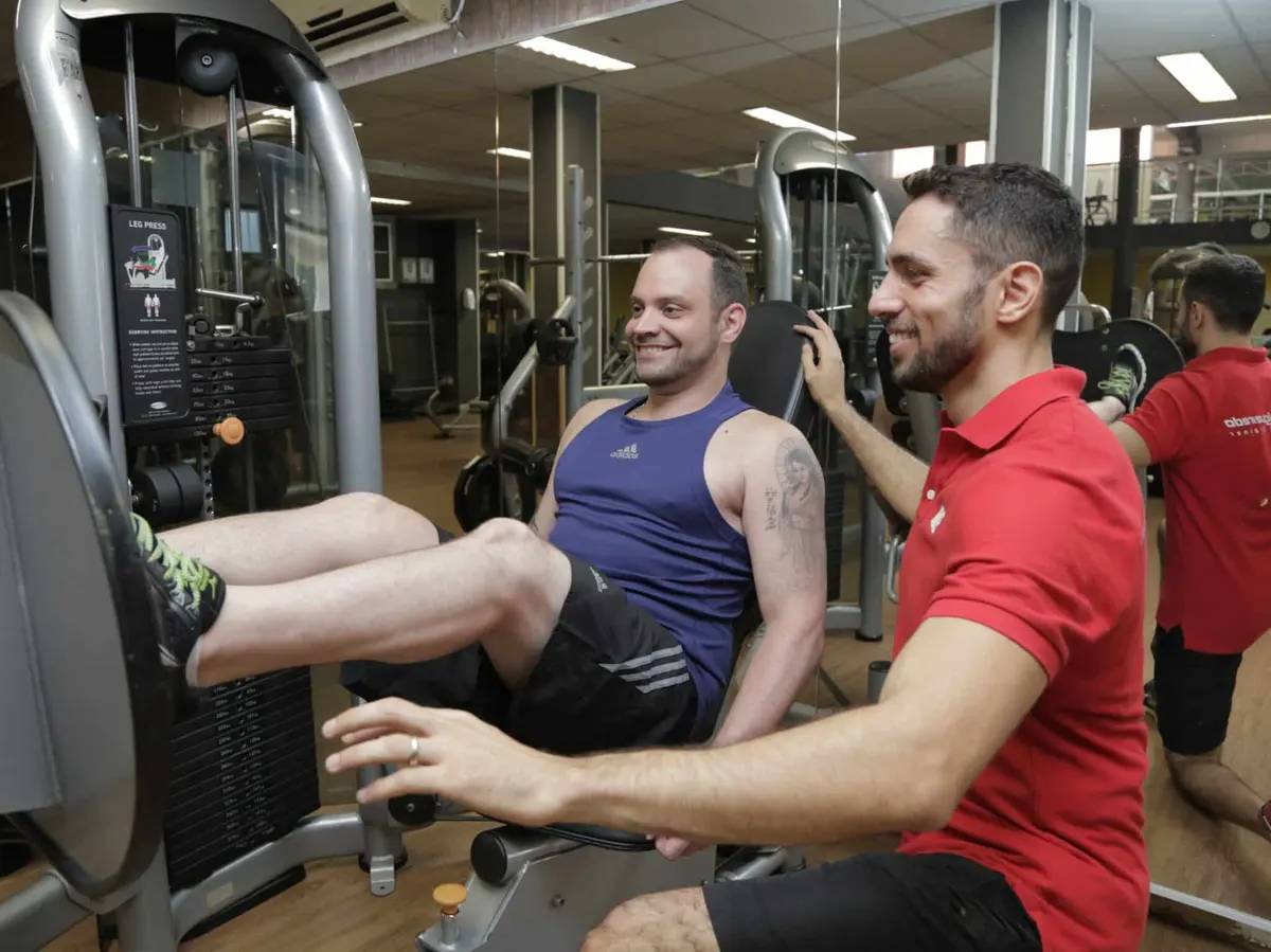 Personal trainer com aluno no leg press