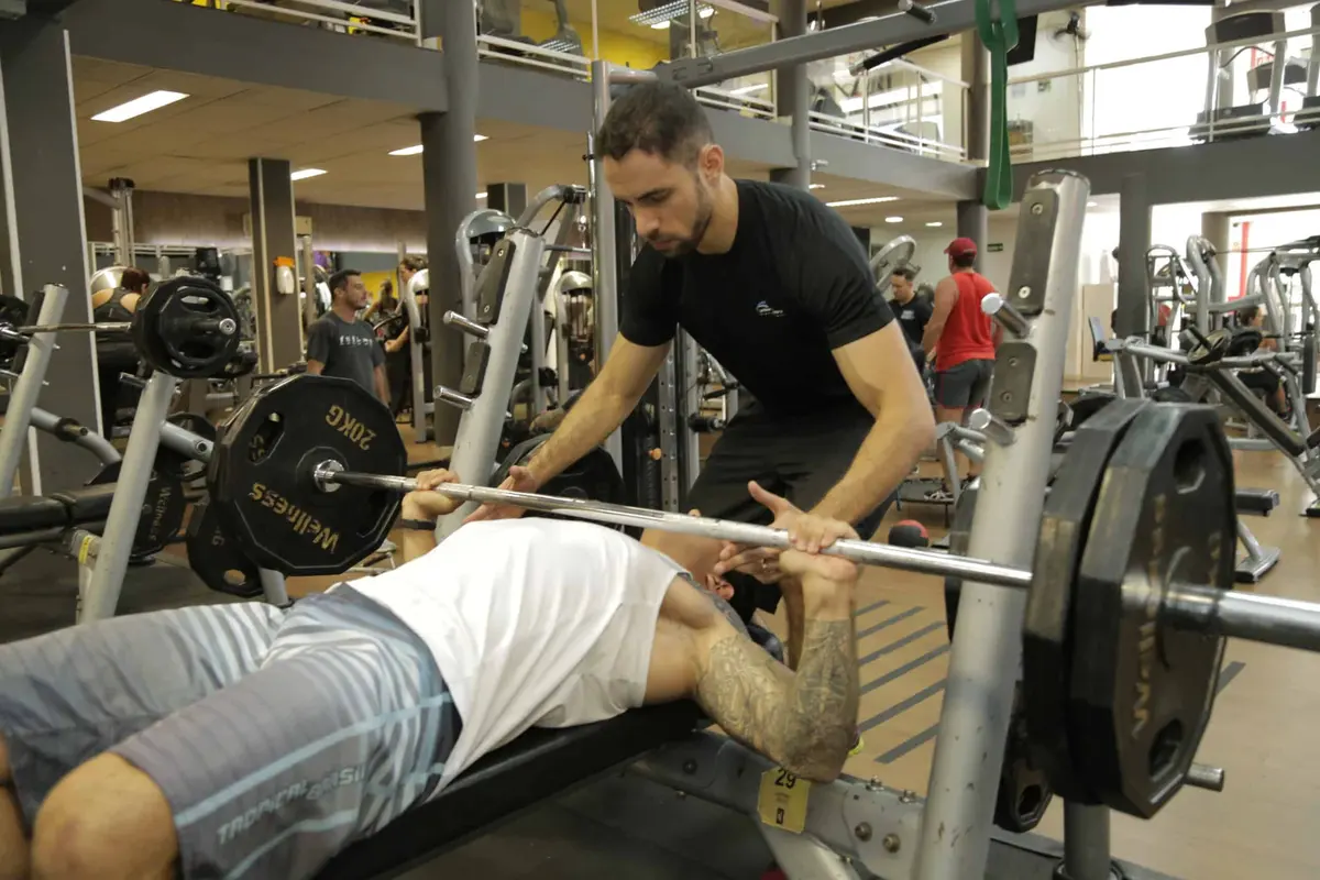 Personal trainer acompanhando aluno no supino