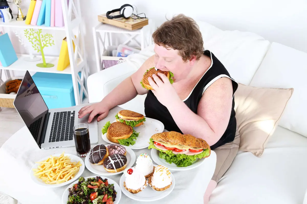 pessoa com obesidade comendo fast food na frente do computador