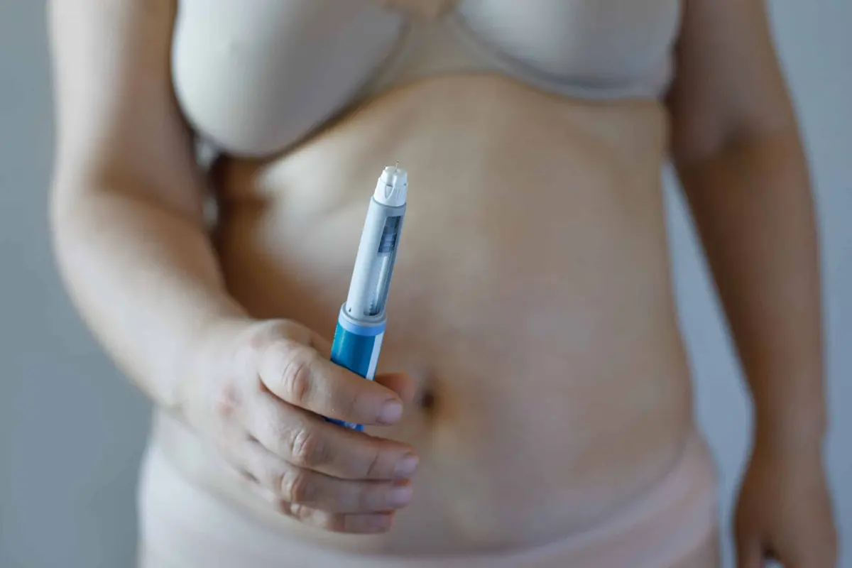 mulher aplicando caneta de medicamento na barriga