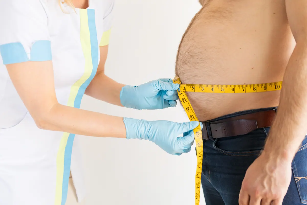 Homem medindo a barriga com fita métrica