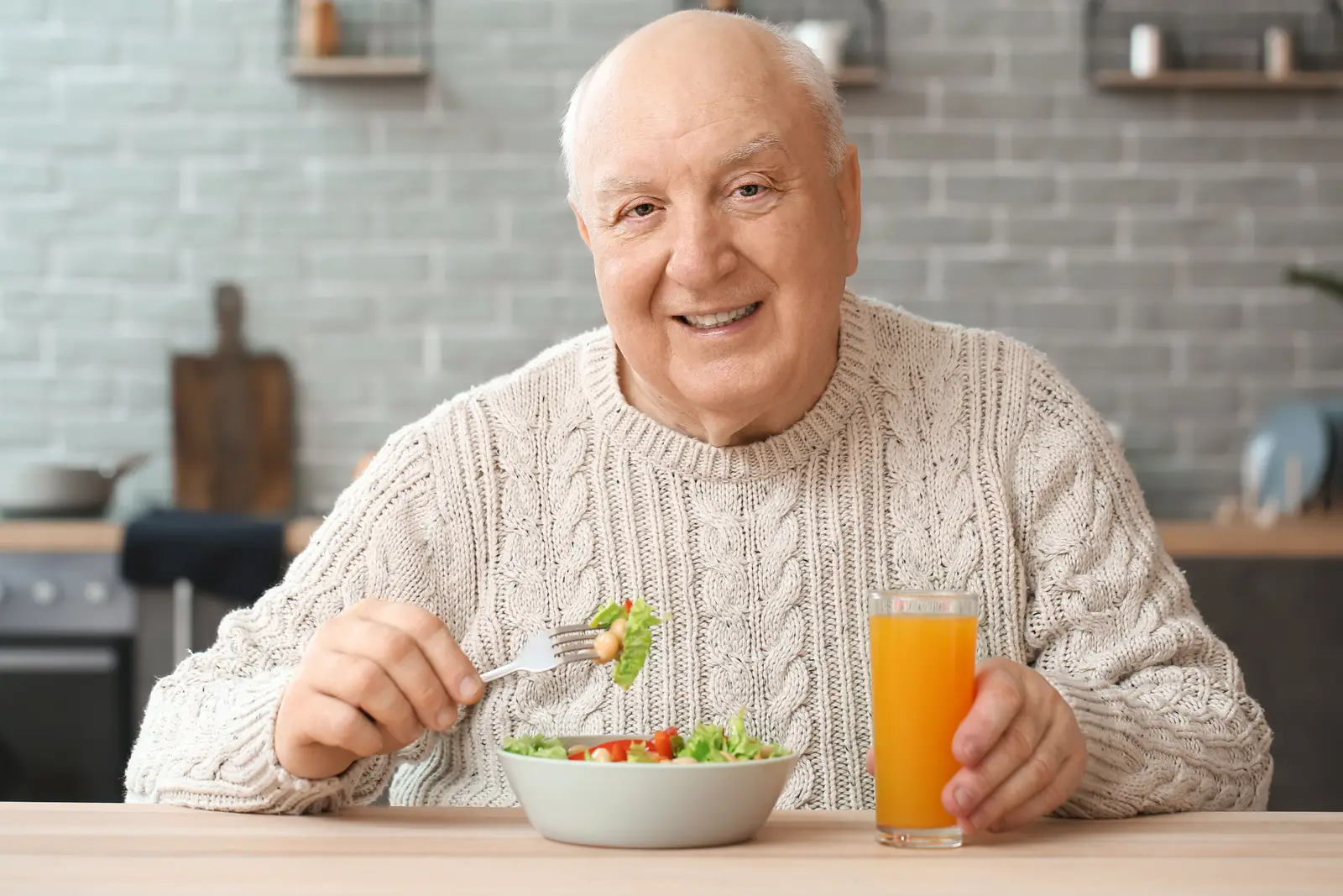 homem idoso sorrindo almoçando salada em casa