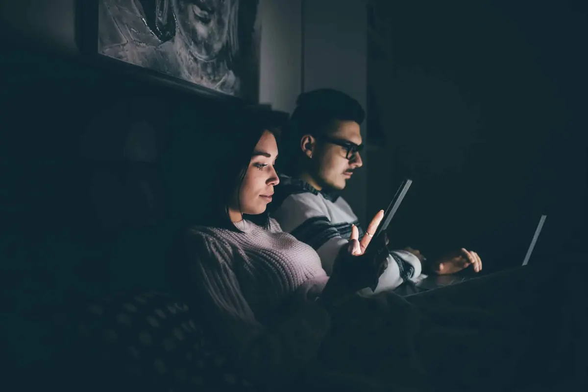 casal usando o celular na cama à noite