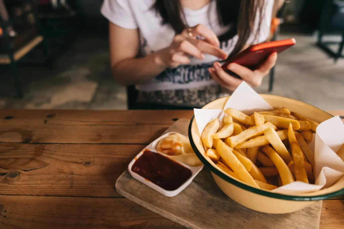 mulher comendo batata frita com smartphone