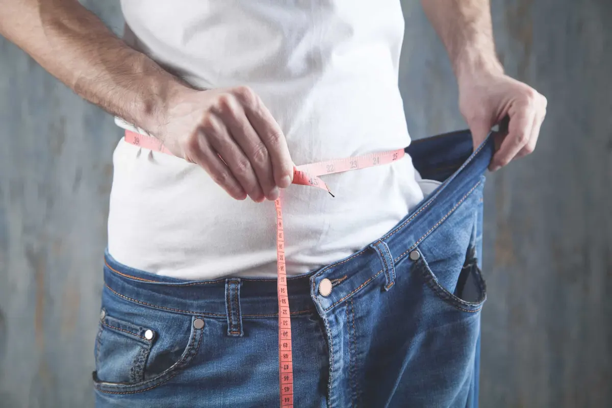 homem mostrando a calça larga depois de emagrecer