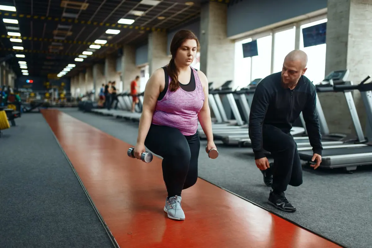 personal trainer orientando mulher no afundo com halteres