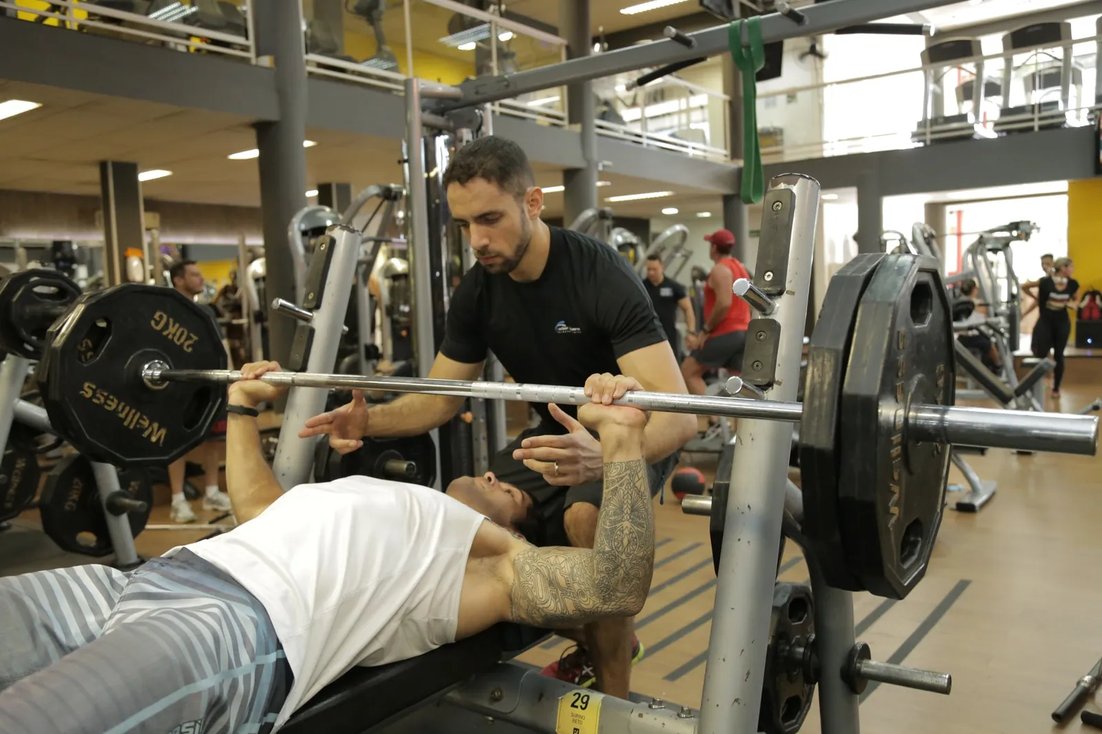 Rafael Figueiredo, personal trainer, acompanhando um aluno no supino com barra