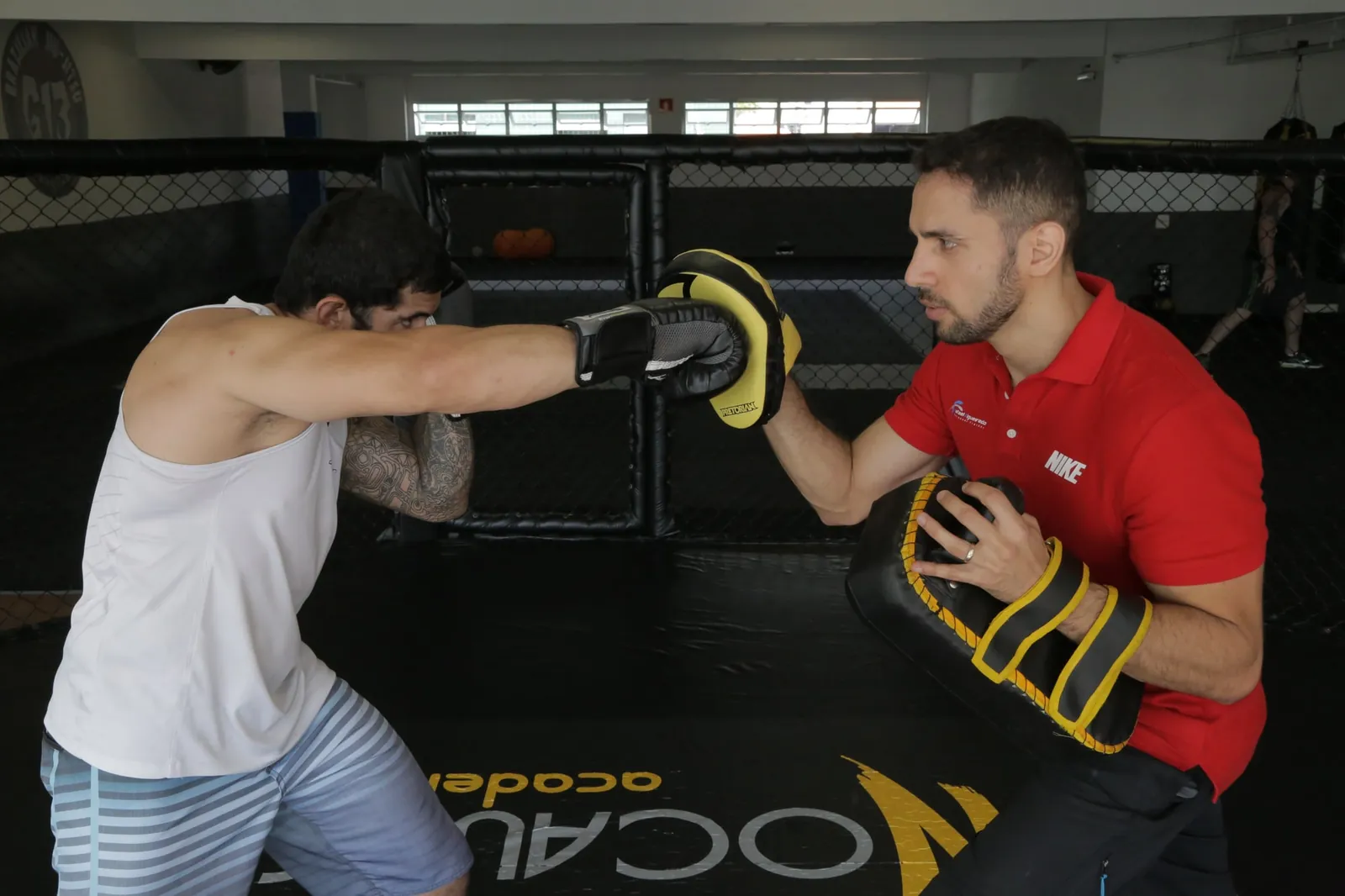 Rafael Figueiredo segurando aparador de soco para um aluno no treino de luta