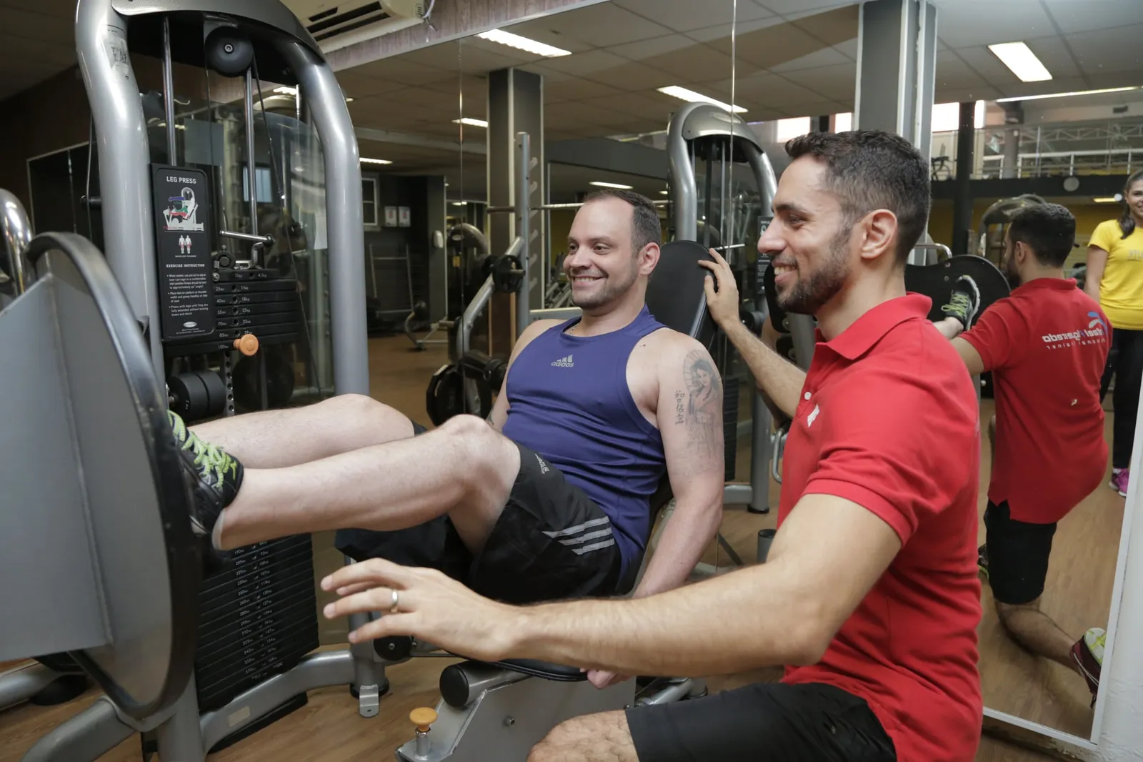 Rafael Figueiredo, personal trainer, acompanhando de perto um aluno no leg press