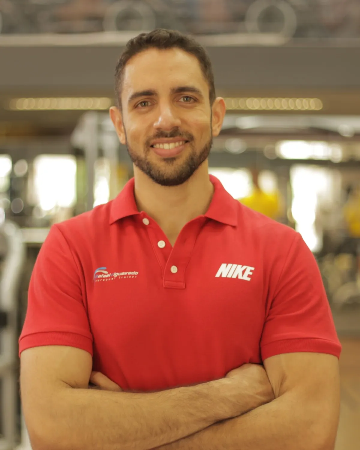 Rafael Figueiredo, personal trainer, de camisa polo vermelha e braços cruzados na academia