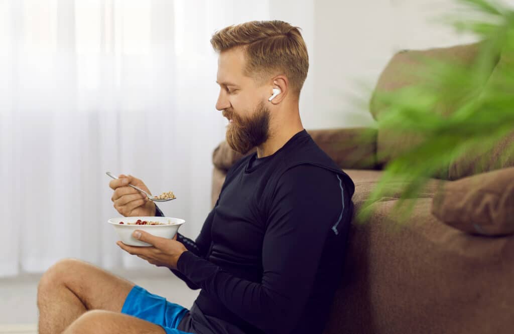 homem comendo lanche pré-treino saudável sentado no sofá