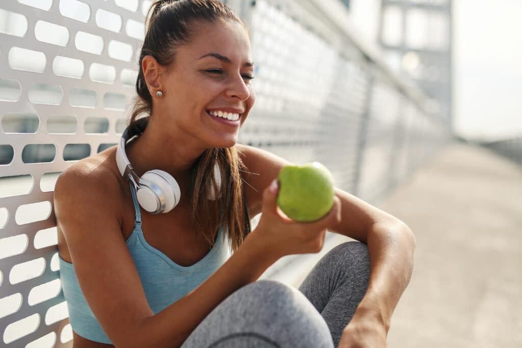 O que comer antes do treino Fit and sporty young woman having break from running and eating apple