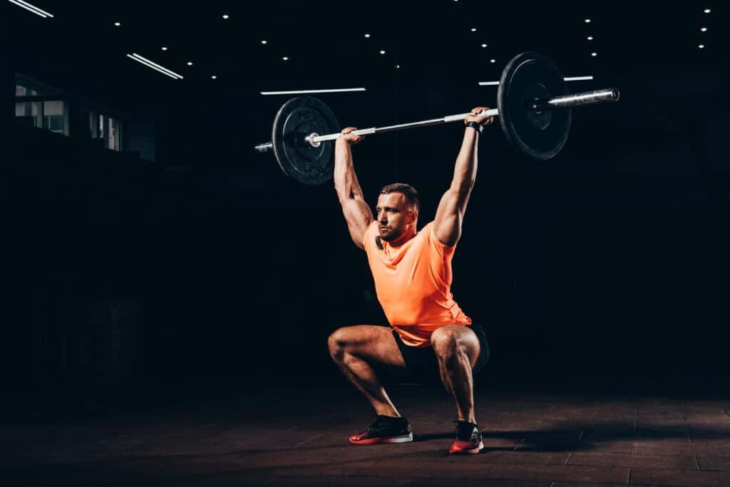 attractive athletic man working out with barbell in dark gym overhead squat snatch